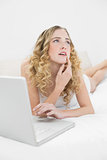 Pretty thoughtful blonde lying on bed using laptop