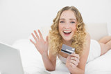 Pretty waving blonde lying on bed using laptop for online shopping