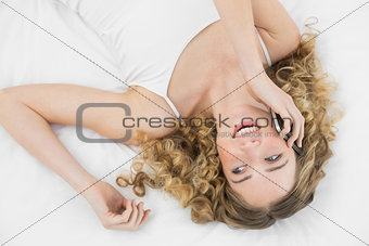 Pretty laughing blonde lying on bed phoning with mobile phone