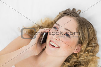 Pretty happy blonde lying on bed phoning with mobile phone