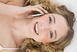 Pretty smiling blonde lying on bed phoning with mobile phone