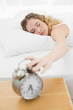 Pretty content blonde lying in bed turning off alarm clock