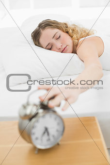 Pretty content blonde lying in bed turning off alarm clock