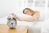 Pretty calm blonde lying in bed turning off alarm clock