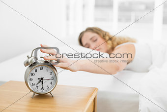Pretty calm blonde lying in bed turning off alarm clock
