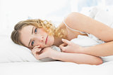 Pretty unsmiling blonde lying in bed resting