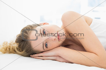 Pretty content blonde lying in bed looking at camera