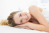 Pretty cheerful blonde lying in bed looking at camera