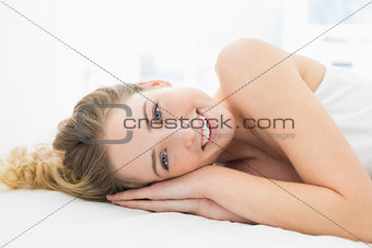 Pretty cheerful blonde lying in bed looking at camera