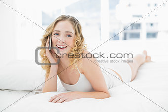 Pretty cheerful blonde lying in bed phoning