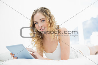 Pretty cheerful blonde lying in bed using tablet