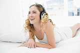 Pretty smiling blonde lying in bed listening to music