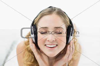 Pretty smiling blonde lying in bed listening to music with closed eyes