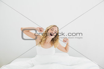 Pretty yawning blonde sitting in bed stretching arms