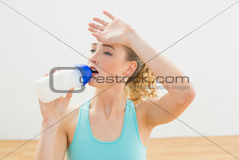 Exhausted slim blonde sitting on floor drinking from sports bottle