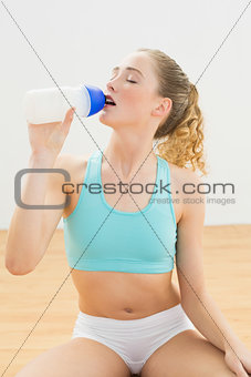 Peaceful slim blonde sitting on floor drinking from sports bottle