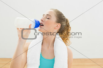 Content slim blonde sitting on floor drinking from sports bottle