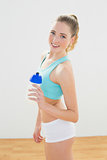 Cheerful slim blonde standing and holding sports bottle