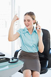 Classy businesswoman on the phone cheering with raised arms