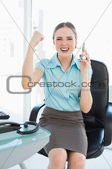 Classy happy businesswoman on the phone cheering with raised arms