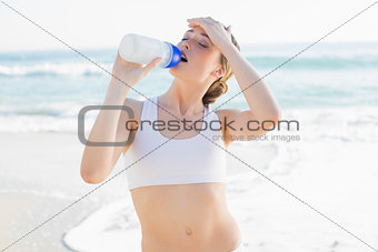 Exhausted slender woman drinking from sports bottle