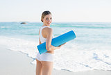 Smiling slender woman holding rolled up exercise mat