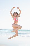 Young woman jumping on the beach wearing a red bikini