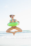 Cute woman holding a rubber ring while jumping on the beach