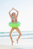 Joyful young woman holding a rubber ring jumping on the beach