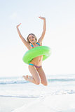 Cheerful young woman holding a rubber ring while jumping on a beach