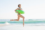 Gorgeous young woman holding a rubber ring while jumping on beach