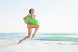 Pretty young woman holding a rubber ring while jumping on beach