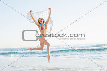 Smiling slender woman jumping in the air holding shawl