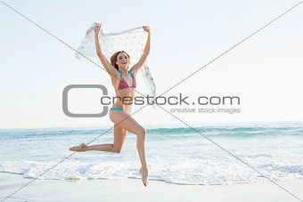 Gleeful slender woman jumping in the air holding shawl