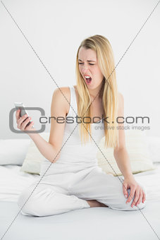 Beautiful blonde woman looking shocked at her smartphone
