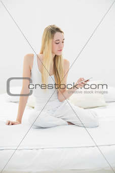 Attractive calm woman using her smartphone sitting on her bed