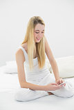 Content calm woman texting with her smartphone sitting on her bed