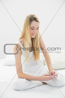 Content calm woman texting with her smartphone sitting on her bed