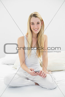 Beautiful calm woman holding her smartphone sitting on her bed