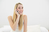 Beautiful calm woman sitting on her bed while phoning