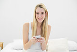 Lovely blonde woman texting with her smartphone sitting on her bed