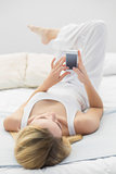 Cute peaceful woman lying on her bed using her smartphone