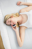 Serious attractive woman phoning with her smartphone lying on her bed