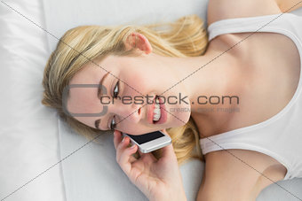 Beautiful woman phoning with her smartphone lying on her bed