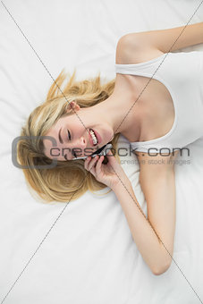 Beautiful young woman phoning with her smartphone lying on her bed