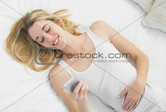 Joyful lovely woman using her smartphone lying on her bed