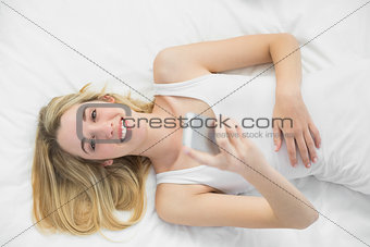 Joyful blonde woman holding her smartphone lying on her bed