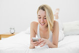 Content young woman texting with her smartphone lying on her bed