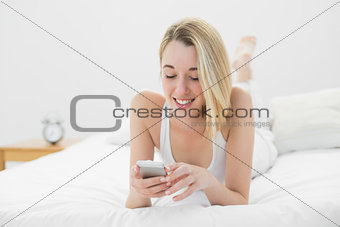 Content young woman texting with her smartphone lying on her bed