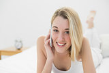Gleeful young woman smiling at camera while phoning with her smartphone